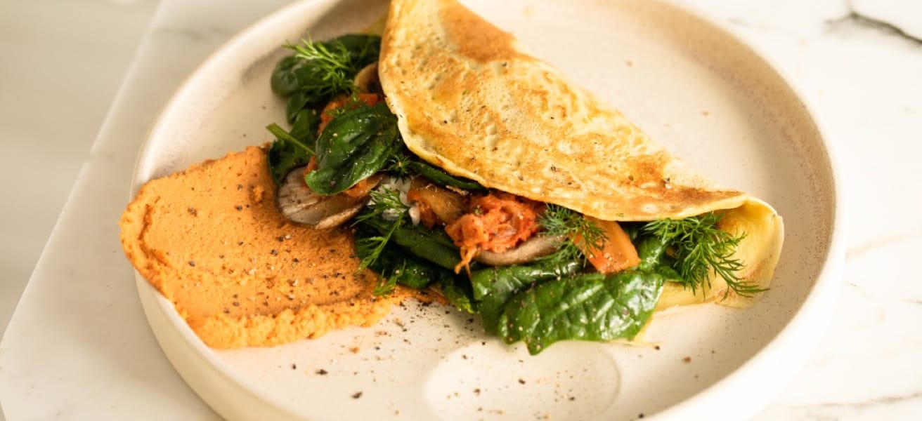 Golden vegetable omelette with pepper, folded and served on a white plate, filled with greens and cheese